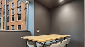 A modern room with a wooden table and two chairs, a window with a view of a building, and a thermostat on the wall. - Student Only Straits Aire (Leeds)