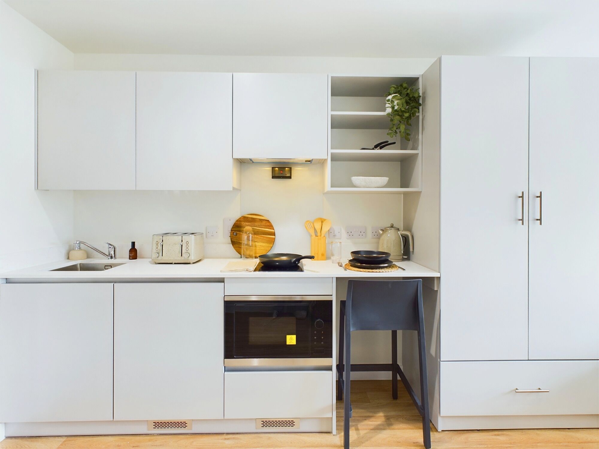 Une cuisine moderne avec des meubles blancs, un four encastré, un micro-ondes et un petit coin repas avec une chaise.
