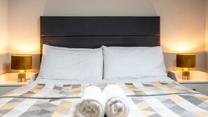 Ein Hotelzimmer mit einem Bett, zwei Nachttischlampen und einem zusammengerollten Handtuch auf dem Bett.