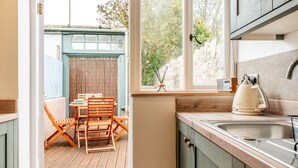 A kitchen with wooden cabinets, a sink, and a window overlooking a garden. - Beautiful One Bedroom Home in Glastonbury (Glastonbury)