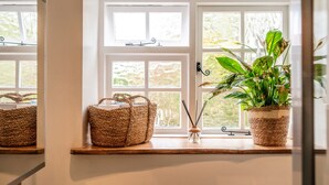 A window with woven baskets on a shelf, a potted plant, and a small vase with reed sticks. - Beautiful One Bedroom Home in Glastonbury (Glastonbury)
