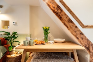 A breakfast setup with croissants, a vase of yellow flowers, and a coffee pot on a wooden table in a room with a sloped ceiling.