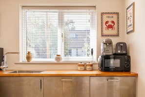 A kitchen with a window, a microwave, a toaster, and two containers labeled 'Tea' and 'Coffee'. - Stunning 1 Bedroom Home in Worcestershire (Hillside)