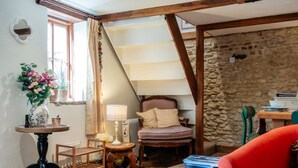 A cozy room with a wooden chair, a small table with a lamp, a bookshelf, and a window with curtains. - Beautiful Two Bedroom Cottage in Oxfordshire (Warborough)