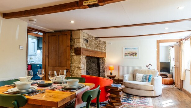 A dining area with a wooden table set for four, a fireplace, a sofa, and a television in a cozy living room. - Beautiful Two Bedroom Cottage in Oxfordshire (Warborough)