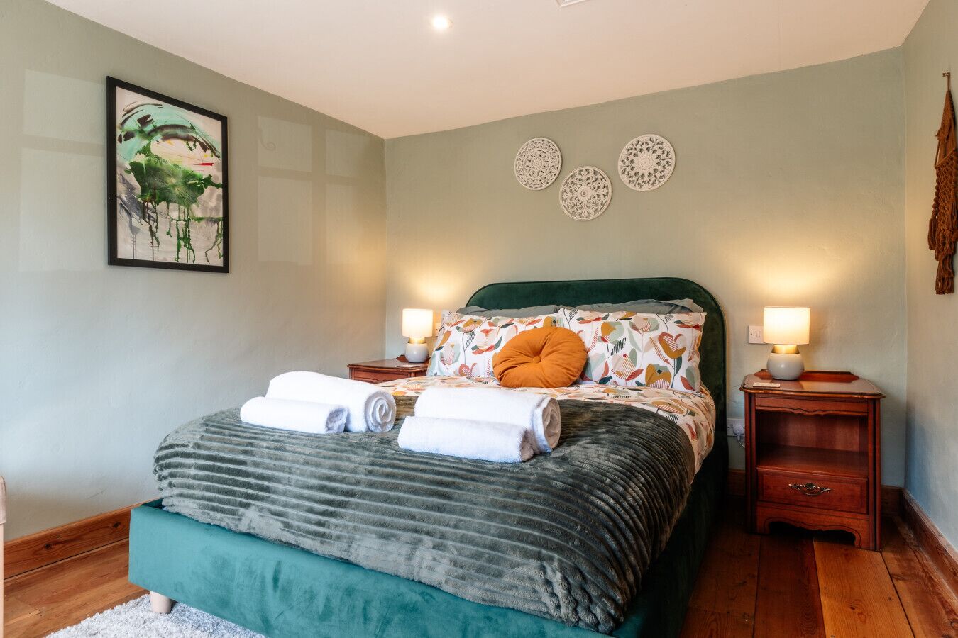 Une chambre à coucher avec un lit, deux tables de chevet, une lampe fixée au mur et un tableau encadré.