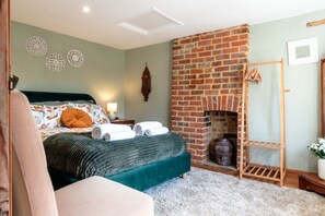 A bedroom with a brick fireplace, a bed with pillows, a bedside table with a lamp, and a wooden ladder.