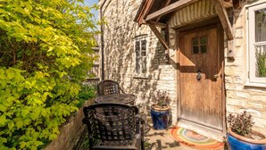 A stone building with a wooden door, a small table with chairs, and potted plants. - Beautiful Two Bedroom Cottage in Oxfordshire (Warborough)