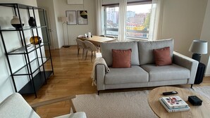 Ein modernes Wohnzimmer mit grauem Sofa, Couchtisch, Bücherregal und Essbereich mit Holztisch und Stühlen.