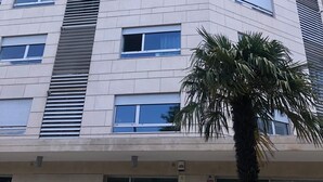 Ein mehrgeschossiges Gebäude mit modernem architektonischen Design, mit einer Reihe von Fenstern und einer Palme im Vordergrund.