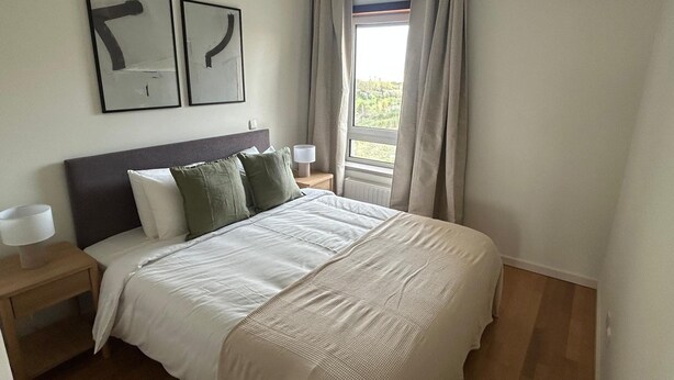 Ein Schlafzimmer mit einem Bett, zwei Nachttischen, einem Fenster mit Vorhängen und zwei abstrakten Wandbildern.