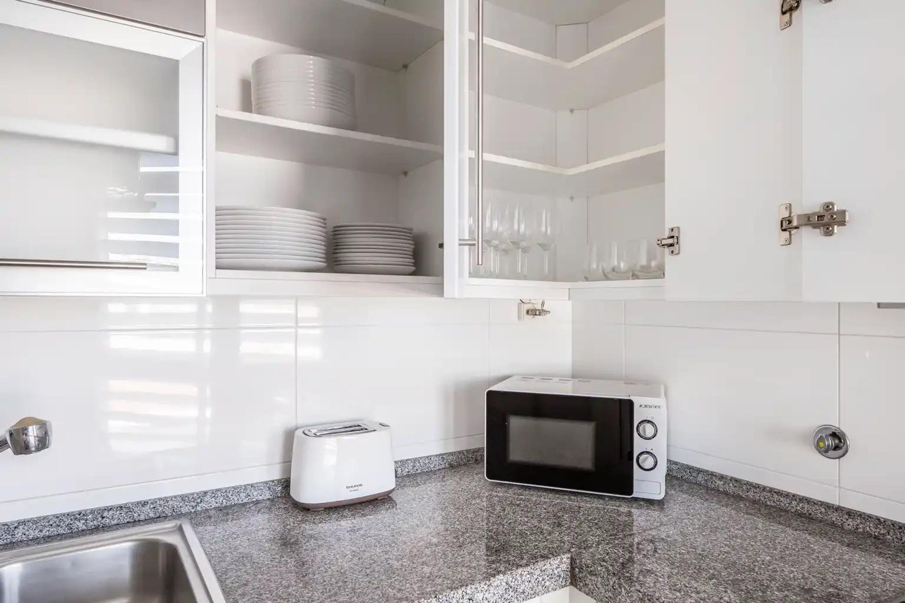 A kitchen with white cabinets, a toaster, a microwave, and shelves with plates and glasses.