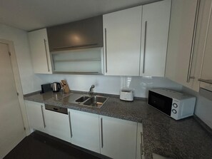 A compact kitchen with white cabinets, a stainless steel sink, a toaster, and a microwave. - Areeiro Elegant by Homing (Lisbon)
