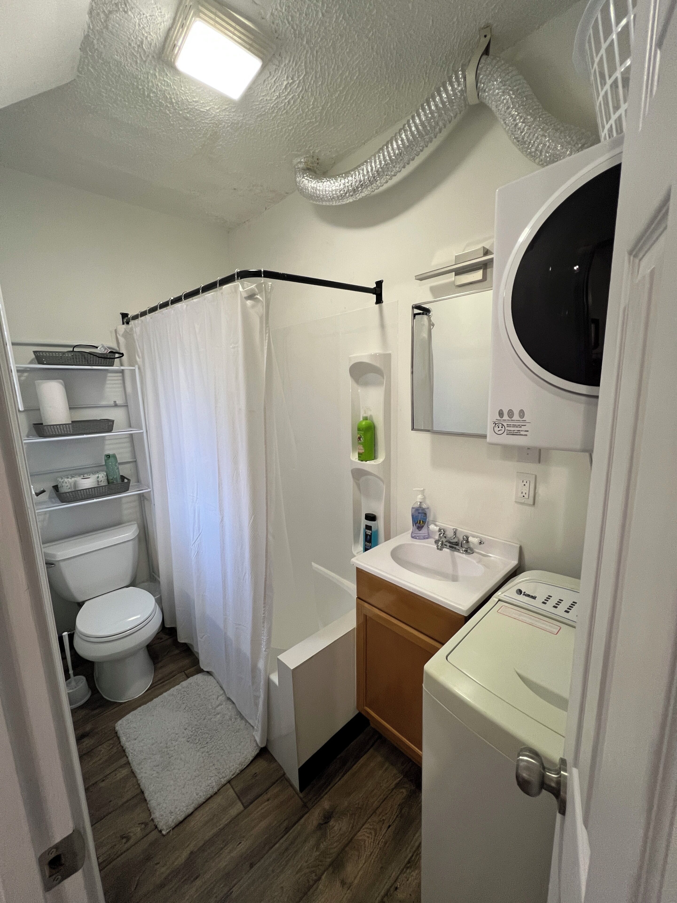 A bathroom with a toilet, shower, sink, and a mirror.