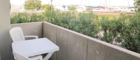 A balcony with a white table and chairs, a view of boats, and greenery.