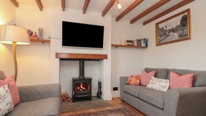 A living room with a fireplace, sofas, a TV, and a patterned rug. - Isla Cottage (Northallerton)