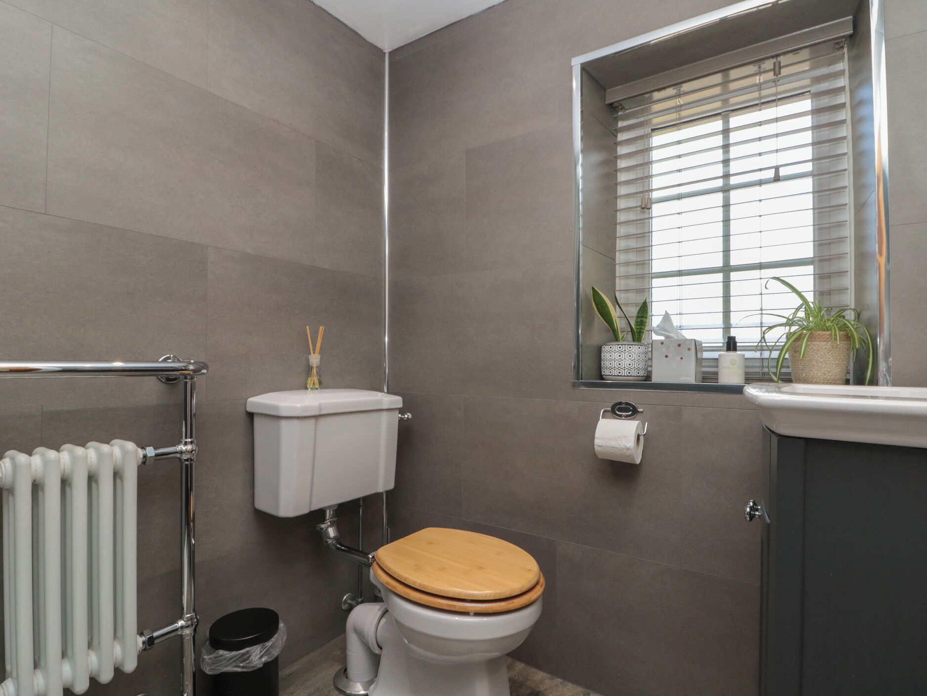 A bathroom with a toilet, radiator, and window with blinds.