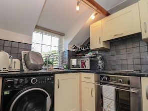 A compact kitchen with a washing machine, a toaster, a microwave, and a stove. - Isla Cottage (Northallerton)