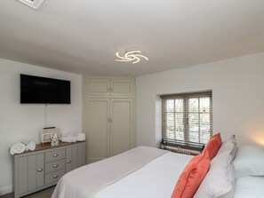 A bedroom with a bed, a dresser, a television, a window with blinds, and a ceiling light.