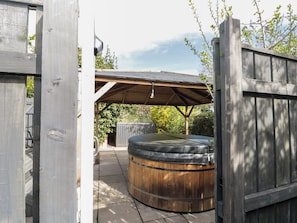 A wooden outdoor hot tub area with a covered roof, a wooden fence, and a stone pathway. - Isla Cottage (Northallerton)