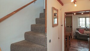 A staircase with wooden handrails, a mirror on the wall, and a doorway leading to a living area with a sofa and a window. - Isla Cottage (Northallerton)