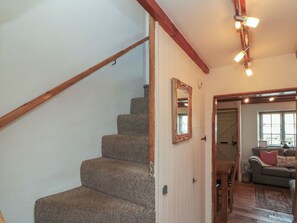 Eine Treppe mit Holzwandläufen, ein Spiegel an der Wand und ein Durchgang zu einem Wohnbereich mit Sofa und Fenster.