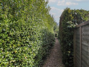 A narrow pathway flanked by dense green foliage and a wooden fence. - Isla Cottage (Northallerton)