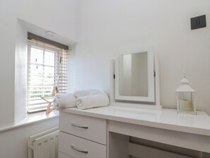 A white bathroom with a window, a mirror, a radiator, and a white candle on the counter.