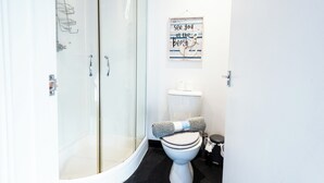 Een badkamer met een douche met glazen wand, een toilet en een aan de muur bevestigd bord.