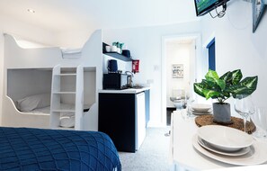 A compact room with a bunk bed, a kitchenette, a dining area with a table set for two, and a potted plant. - Guestz at The Wellington (Blackpool)