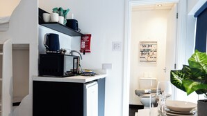 Een kleine keuken met een koffiezetapparaat, magnetron en een plank met keukengerei.