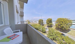 Ein Balkon mit Blick auf einen Yachthafen, ein weißer Tisch mit einem Buch und ein Stuhl.