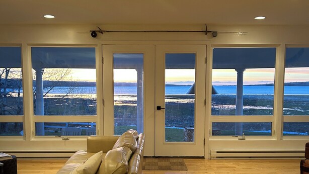 Un salón amplio con un sofá grande, suelo de madera y ventanas grandes que ofrecen vistas al paisaje.