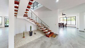 Un interior espacioso con una escalera moderna, un comedor y ventanas amplias.