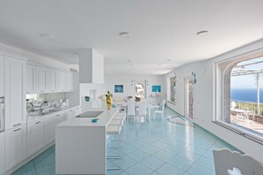 Eine moderne Küche mit weißen Schränken, einer zentralen Kochinsel und Meerblick durch große Fenster.