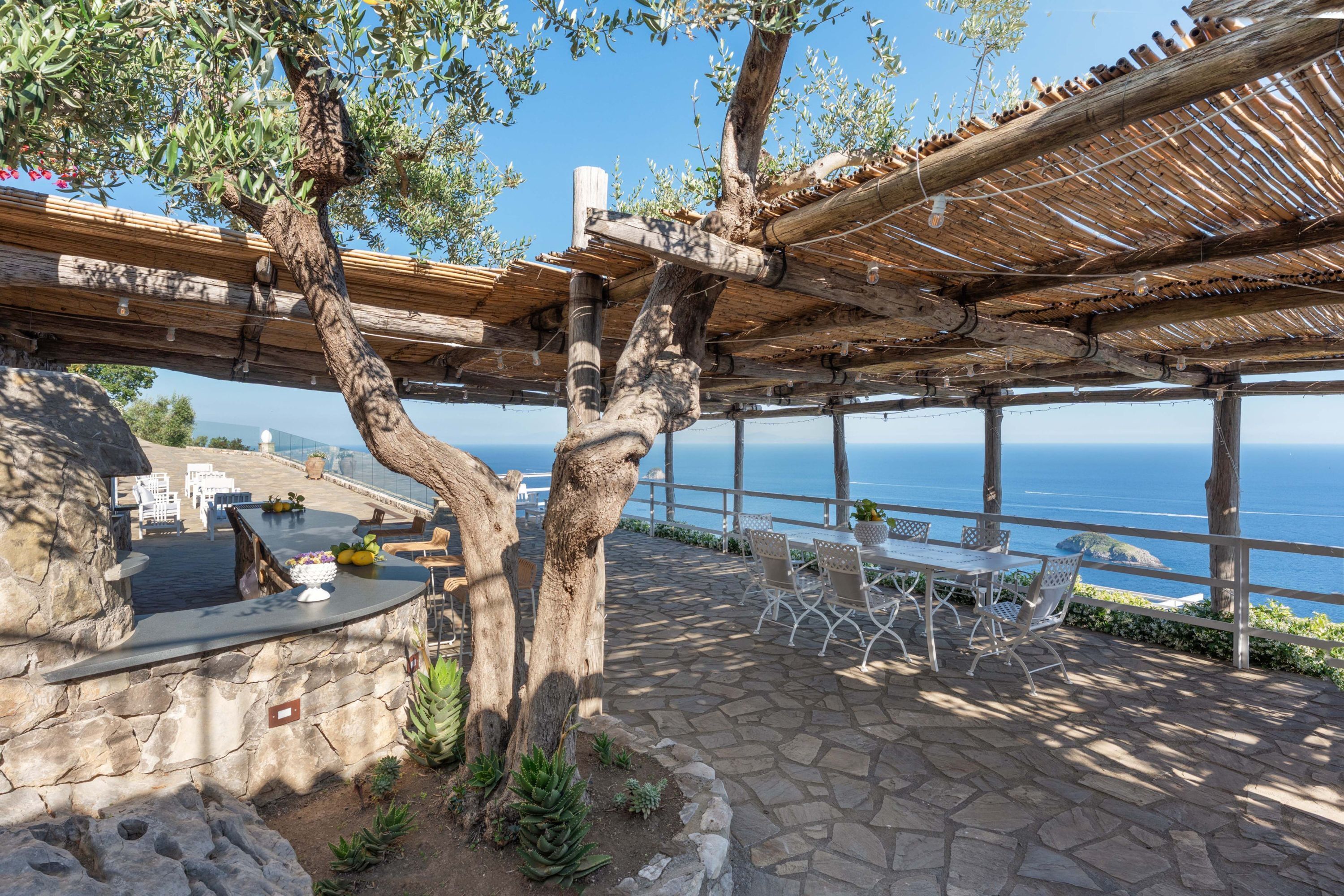 Eine Steinterrasse mit Außenmöbeln, einer Pergola und Meerblick.