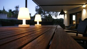 Ein Holztisch mit zwei Lampen unter einer überdachten Terrasse.