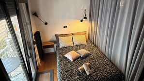 Un dormitorio con una cama, una mesita de noche, una lámpara y vistas a través de un ventanal corredero.