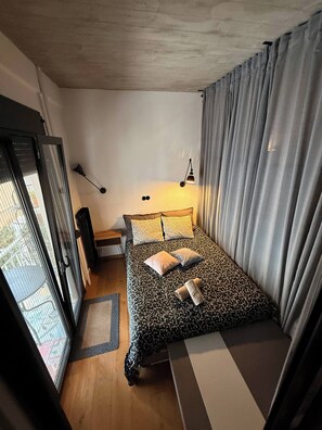 A bedroom with a bed, a nightstand, a lamp, and a view through a sliding door. - Wyn-cozy Studiostniarchos Foundation Near the Sea (Kallithea)