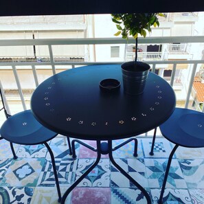 A round table with two chairs, a potted plant, and a small ashtray on a balcony with patterned tiles and a railing. - Wyn-cozy Studiostniarchos Foundation Near the Sea (Kallithea)