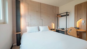 Une chambre d’hôtel moderne avec un grand lit, une tête de lit en bois, un bureau avec une chaise et un miroir.