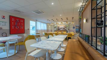 Un café moderno con mesas redondas, sillas amarillas y un letrero de salida rojo.
