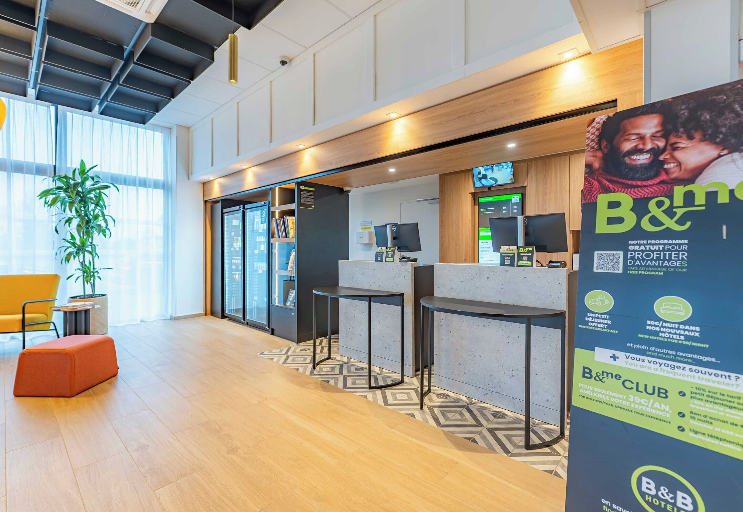 Un moderno vestíbulo de hotel con mostrador de recepción, zona de estar y un gran cartel publicitario del B&B Club.