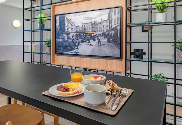 Bandeja de desayuno con huevos, salchicha, tostadas y jugo sobre una mesa con un marco que contiene una fotografía de una escena callejera.