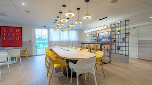 Une salle de conférence avec une longue table, des chaises jaunes et des luminaires suspendus.