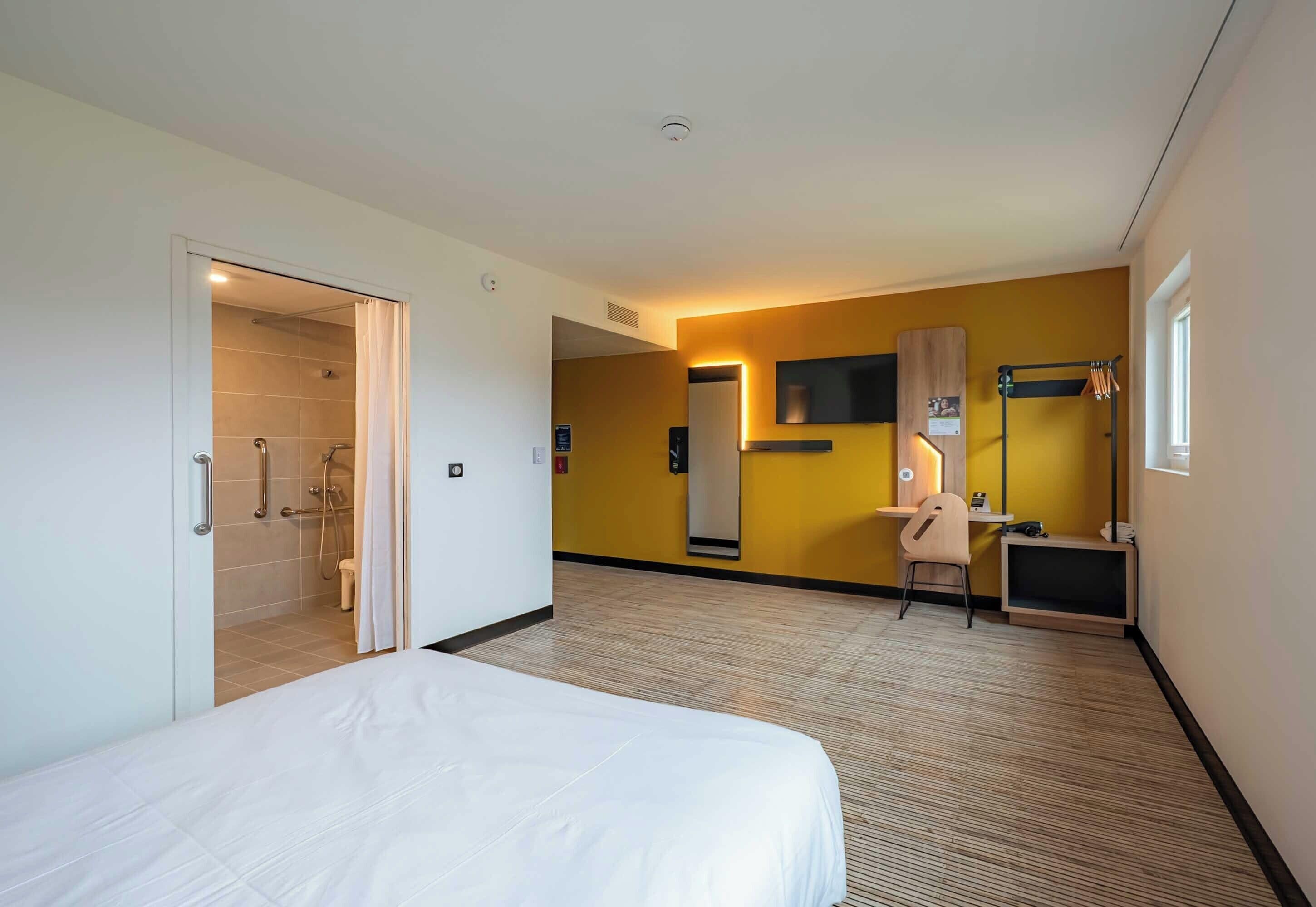 Een hotelkamer met een bed, een bureau, een stoel, een televisie en een douche.