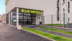 Un hôtel-chambre d’hôtes moderne avec une façade en verre, un parking clos et un ciel dégagé.