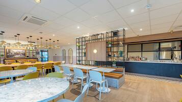 Una cafeteria moderna amb taules de marbre, cadires grogues i blanques, un taulell de fusta i un gran finestral.