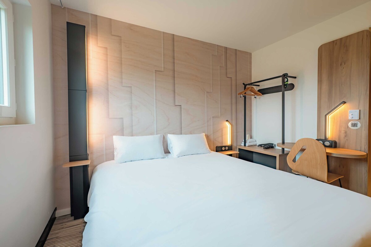 Et moderne hotelværelse med en stor seng, et træsengegærde, et skrivebord med stol og et spejl.