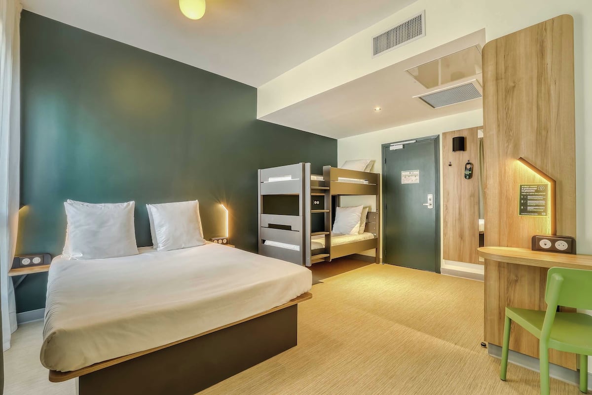 A hotel room with a bed, a desk, a chair, a wardrobe, and a door.